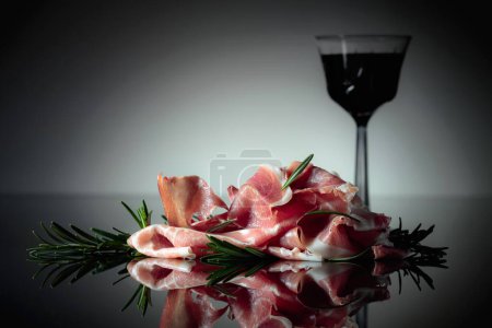 Téléchargez les photos : Prosciutto italien ou jamon espagnol au romarin et vin rouge sur fond noir. - en image libre de droit