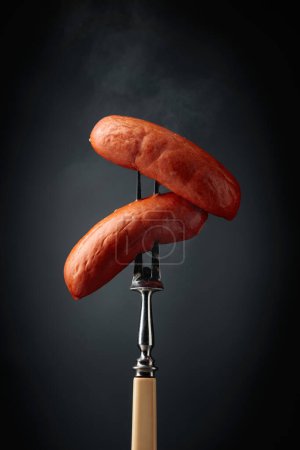 Foto de Salchichas hervidas en un tenedor. Salchichas calientes con humo sobre fondo negro. - Imagen libre de derechos