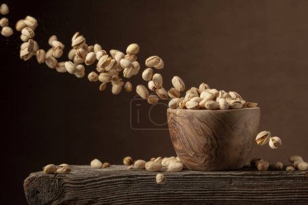 Photo for Flying salted pistachios. Dried nuts in a wooden bowl. Copy space. - Royalty Free Image