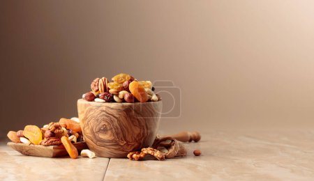 Photo for Dried fruits and nuts on a beige ceramic table. The mix of nuts, apricots, and raisins in a wooden bowl. Copy space. - Royalty Free Image