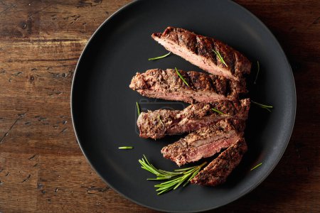 Téléchargez les photos : Bifteck de bœuf côtelé grillé au romarin sur une assiette noire. - en image libre de droit