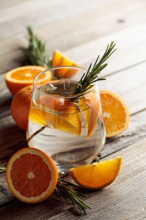 Foto de Tónico de ginebra con hielo, romero y rodajas de naranja en vidrio esmerilado. Cóctel con ingredientes en una vieja mesa de madera. Copiar espacio. - Imagen libre de derechos