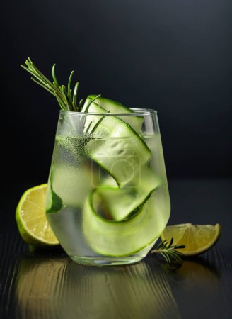 Foto de Gin tonic con hielo, romero, lima y pepino en vidrio esmerilado. Vaso con un cóctel sobre fondo negro. - Imagen libre de derechos