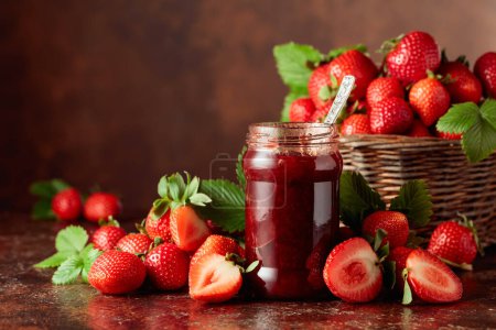 Strawberry jam and fresh berries with leaves on an old brown table. Copy space.