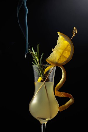 Téléchargez les photos : Limoncello dans un verre. Une liqueur de citron italienne sucrée, une boisson alcoolisée forte traditionnelle garnie d'une branche de romarin fumante. - en image libre de droit
