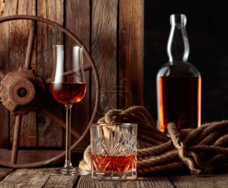 Foto de Cristal, snifter y botella con ron, coñac o whisky sobre un fondo de madera viejo. - Imagen libre de derechos