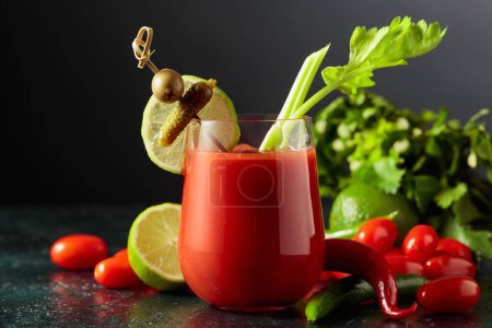 Foto de Cóctel Bloody Mary decorado con pepinillo, olivo, lima y apio. Bebida de tomate con ingredientes sobre fondo negro. - Imagen libre de derechos