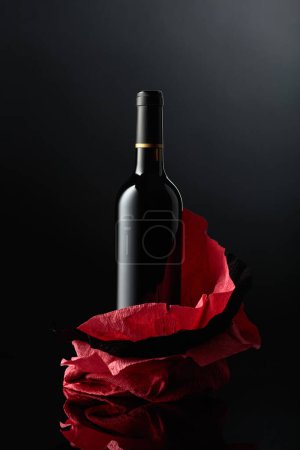 Foto de Bottle of red wine on a crumpled paper. Black reflective background. - Imagen libre de derechos