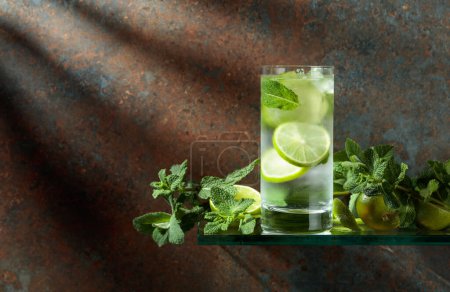 Photo for Mojito with ice, lime, and mint. Iced drink in a misted glass on a rusty background. Copy space. - Royalty Free Image