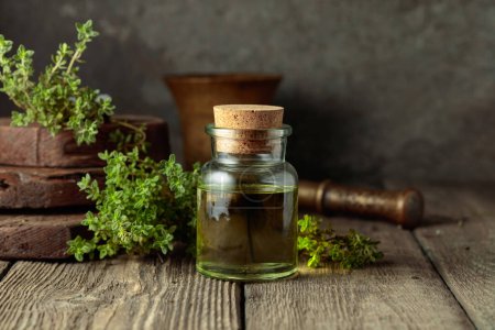 Photo for Bottle of thyme essential oil with fresh thyme twigs on an old wooden table. - Royalty Free Image
