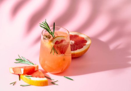 Photo for Summer cocktail with grapefruit, rosemary, and ice. Drink on pink background with palm leaf shadow. Summer, tropical, fresh cocktail concept. - Royalty Free Image