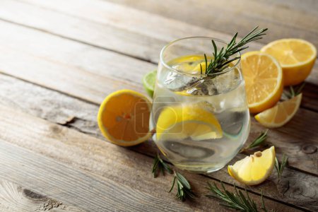 Photo for Gin tonic with ice, rosemary, and lemon slices in frosted glass. Cocktail with ingredients on an old wooden table. Copy space. - Royalty Free Image