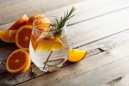 Téléchargez les photos : Gin tonic avec glace, romarin et tranches d'orange en verre dépoli. Cocktail avec des ingrédients sur une vieille table en bois. Espace de copie. - en image libre de droit