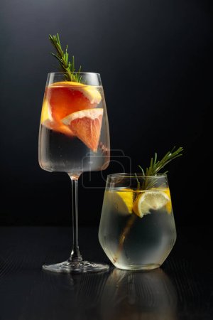 Photo for Gin tonic with ice, rosemary, lemon, and grapefruit in frosted glasses. Glasses with cocktails on a black wooden table. Copy space. - Royalty Free Image