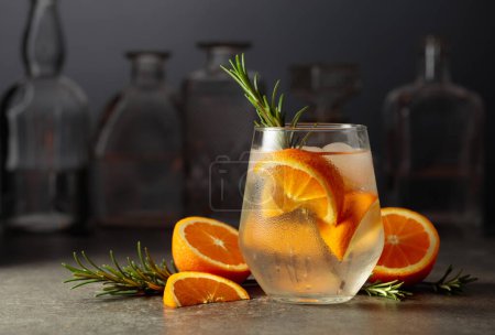 Photo for Cocktail gin tonic with ice, rosemary, and orange on a stone table in a bar. - Royalty Free Image