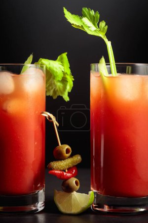 Foto de Cóctel Bloody Mary con apio, pepinillo, aceituna, lima y pimiento rojo. Bebida de tomate sobre fondo negro. - Imagen libre de derechos