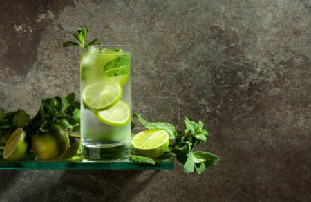 Photo for Mojito with ice, lime, and mint. Iced drink in a misted glass on an old stone background. Copy space. - Royalty Free Image