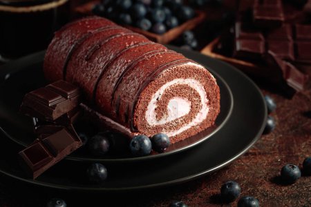 Foto de Pastel de rollo de chocolate con arándanos y una barra de chocolate negro roto. - Imagen libre de derechos
