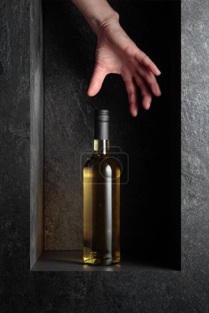 Photo for Hand reach for a bottle of white wine. A concept image on the theme of expensive wines. - Royalty Free Image