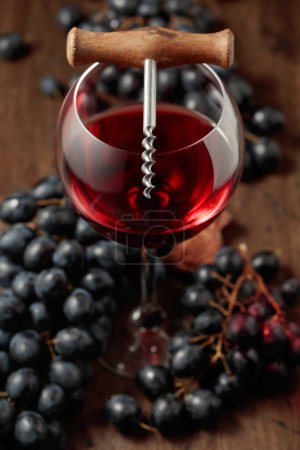 Photo for The glass of red wine, corkscrew, and blue grapes is on an old wooden table. Selective focus. - Royalty Free Image
