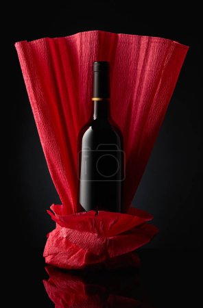 Photo pour Une bouteille de vin rouge sur un papier froissé. Fond réfléchissant noir. - image libre de droit