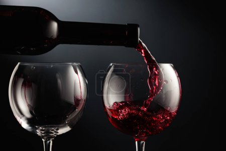 Foto de Verter vino tinto en una copa de vino sobre un fondo negro. - Imagen libre de derechos