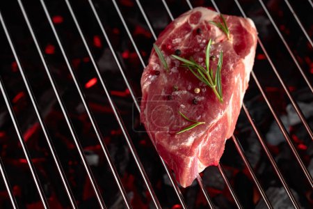 Foto de Raw steak on a grill with rosemary, pepper, and salt. - Imagen libre de derechos