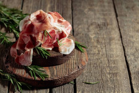 Photo for Italian prosciutto or Spanish jamon with rosemary on an old wooden table. Copy space. - Royalty Free Image