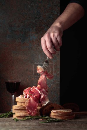 Photo for Prosciutto with bread and rosemary on an old wooden table. Traditional Mediterranean food. Copy space. - Royalty Free Image