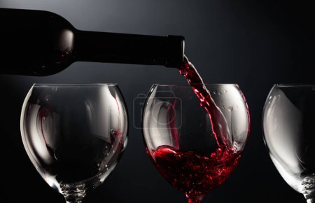 Photo for Pouring red wine into a wine glass on a black background. - Royalty Free Image
