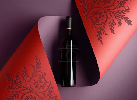 Photo for Bottle of red wine on a paper background with floral ornament. Copy space for your text, top view. - Royalty Free Image