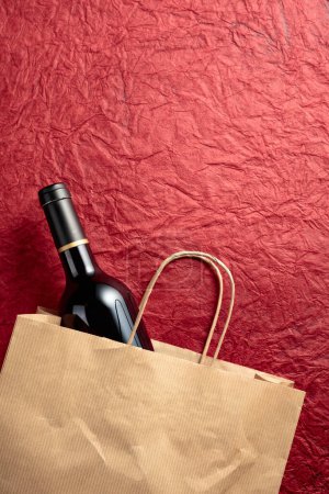 Téléchargez les photos : Sac à provisions en papier avec une bouteille de vin rouge sur fond rouge texturé. Vue du dessus, espace de copie. - en image libre de droit
