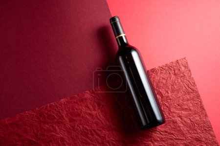 Téléchargez les photos : Bouteille de vin rouge sur fond rouge.Fond rouge avec différentes textures et nuances. Vue du dessus, espace de copie. - en image libre de droit