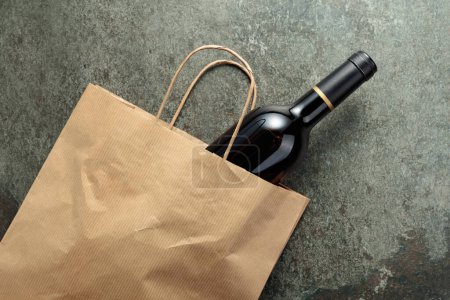 Foto de Bolsa de compras de papel con una botella de vino tinto sobre un viejo fondo de piedra. Vista superior, espacio de copia. - Imagen libre de derechos