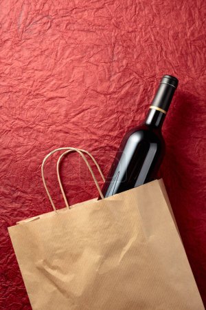 Téléchargez les photos : Sac à provisions en papier avec une bouteille de vin rouge sur fond rouge texturé. Vue du dessus, espace de copie. - en image libre de droit