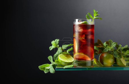 Téléchargez les photos : Cocktail Cuba Libre au rhum brun, cola, menthe et citron vert. Boisson glacée dans un verre embrumé sur fond noir. Espace de copie. - en image libre de droit