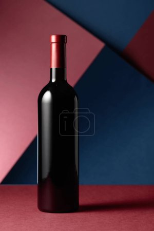 Téléchargez les photos : Une bouteille de vin rouge sur fond rouge-bleu. Espace de copie - en image libre de droit