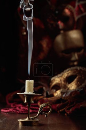 Foto de Bodegón con una vela apagada en un viejo candelero de latón y máscaras de carnaval. - Imagen libre de derechos