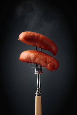 Photo for Boiled sausages on a fork. Hot sausages with smoke on a black background. - Royalty Free Image
