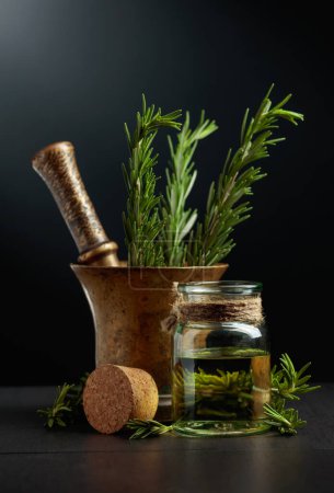 Photo for Bottle of rosemary aromatherapy oil extract with fresh rosemary branches and old brass mortar. - Royalty Free Image
