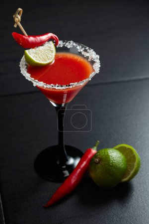 Foto de Cóctel Bloody Mary con lima y pimienta roja sobre fondo negro. El vidrio está decorado con sal marina. - Imagen libre de derechos