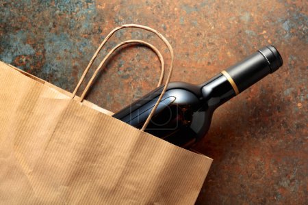 Photo for Paper shopping bag with a bottle of red wine on a rusty metal background. Top view, copy space. - Royalty Free Image