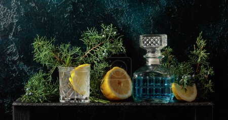 Foto de Cóctel gin-tonic con hielo, limón y romero en un vaso congelado. Una bebida refrescante con ramas de enebro sobre un fondo vintage azul oscuro. Copiar espacio. - Imagen libre de derechos