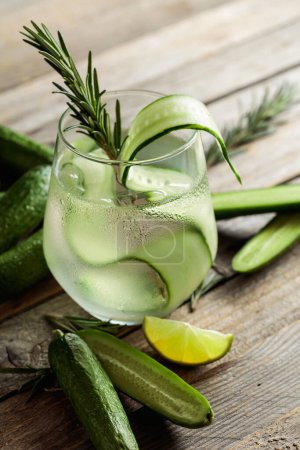 Photo for Gin tonic with ice, rosemary, lime, and cucumber slices in frosted glass. Cocktail with ingredients on an old wooden table. - Royalty Free Image