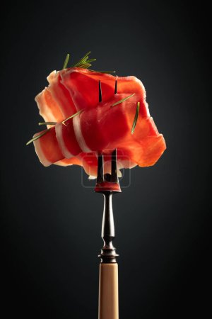 Photo for Sliced prosciutto with rosemary on a fork. - Royalty Free Image