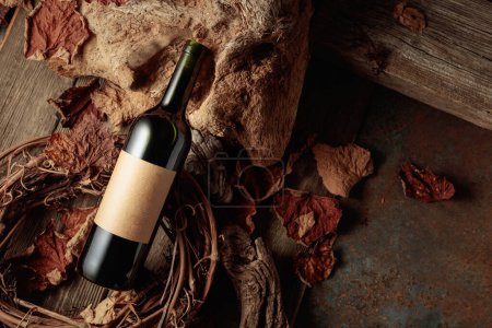 Photo for Bottle of red wine with a blank old label. Vintage rustic background with old wood and dried-up vine leaves. Concept of old wine. - Royalty Free Image