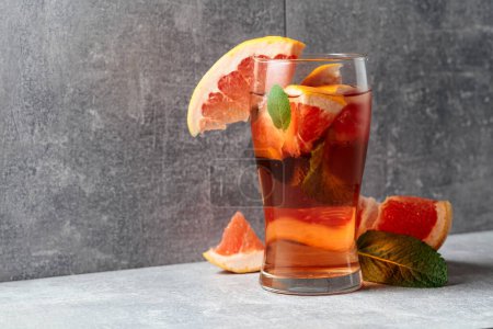 Photo for Iced tea with ice, mint, and grapefruit. A cold refreshing drink with ingredients on a grey background. Copy space. - Royalty Free Image