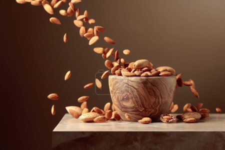 Téléchargez les photos : Les noix d'amande sont versées dans un bol en bois. Fond brun avec espace de copie. - en image libre de droit