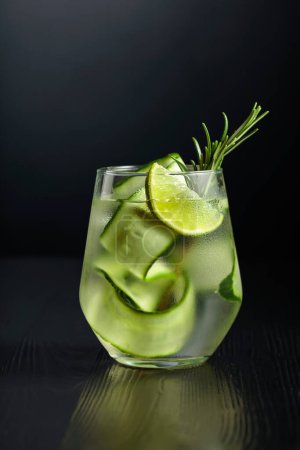 Photo for Gin tonic with ice, rosemary, lime, and cucumber in frosted glass. Glass with a cocktail on a black background. Copy space. - Royalty Free Image