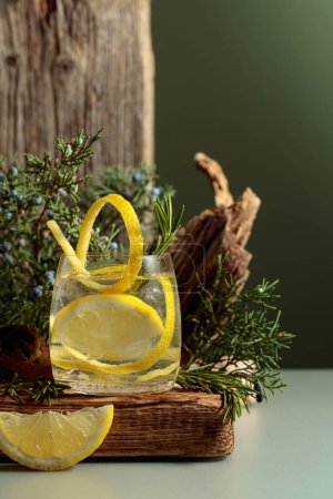 Foto de Cóctel gin-tonic con hielo, limón y romero en un vaso congelado. Una bebida refrescante con ramas de enebro y enganches en un tablón viejo. - Imagen libre de derechos